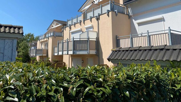 A row of residential buildings with balconies, a tiled roof, and a clear blue sky. - Vacation apartment Strandwiese 3 (Graal-Müritz)
