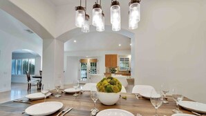 A dining area with a wooden table set for six, white plates, silverware, and a centerpiece of green vegetables. - Specials! Heated pool+spa|Game room|Sports courts (Thousand Palms)