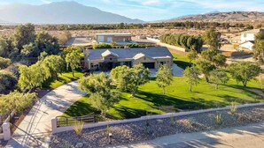 A residential property with a large house, a well-maintained lawn, and a mountain backdrop. - Specials! Heated pool+spa|Game room|Sports courts (Thousand Palms)