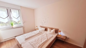 Een slaapkamer met een bed, nachtkastje, raam en radiator.
