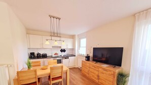 Een moderne keuken met witte kastjes, een eettafel met stoelen, een grote flatscreen-tv en een potplant.