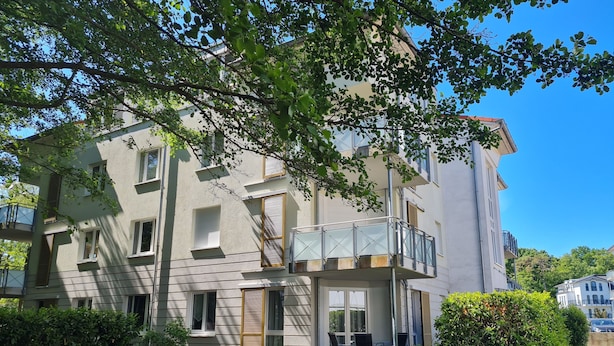 Een meerlaags woongebouw met balkons, een kleine tuin en een heldere lucht.