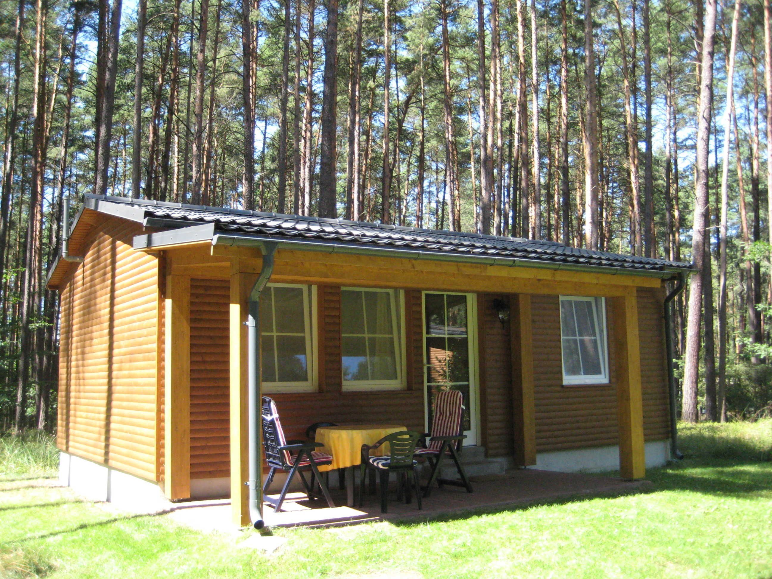 A small wooden cabin with a porch, two windows, and a table with chairs.