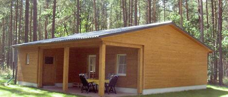 Una baita di legno con un portico coperto, due finestre e un tavolo con sedie.
