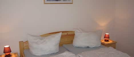 A neatly made bed with white linens, two pillows, and a wooden headboard. There are two bedside tables with lamps, and a framed picture hangs on the wall above the bed.