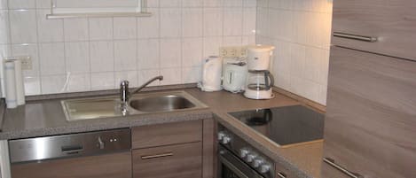 Eine moderne Küche mit Spüle aus Edelstahl, integriertem Backofen, Kaffeemaschine und einem Fenster über der Spüle.