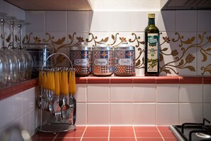 Une cuisine avec un mur recouvert de carreaux, une bouteille d’huile d’olive et des récipients étiquetés pour le café, le sucre et le sel.