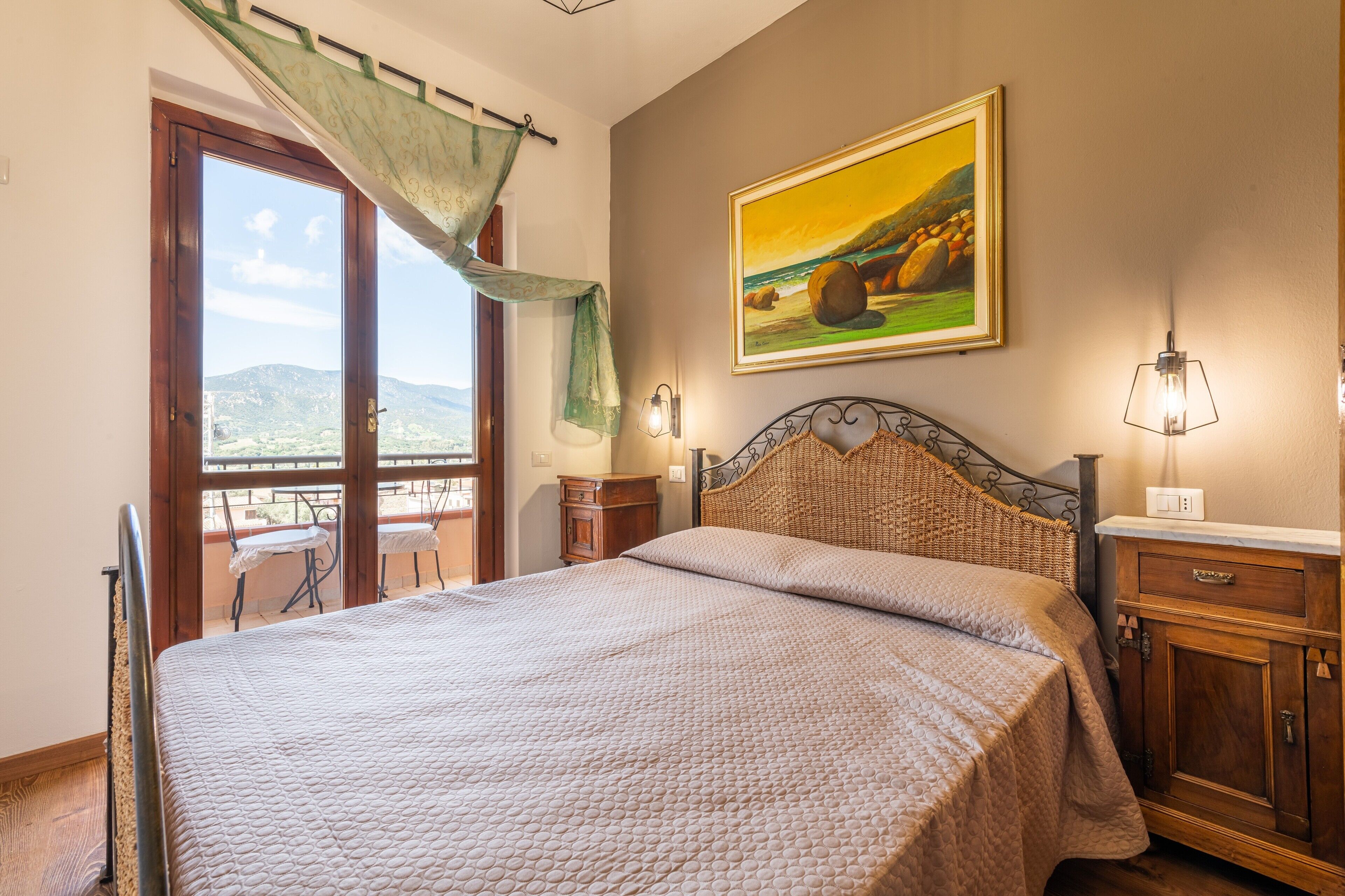 Une chambre avec un grand lit, une vue à travers une porte vitrée, un tableau au mur et une table de chevet.