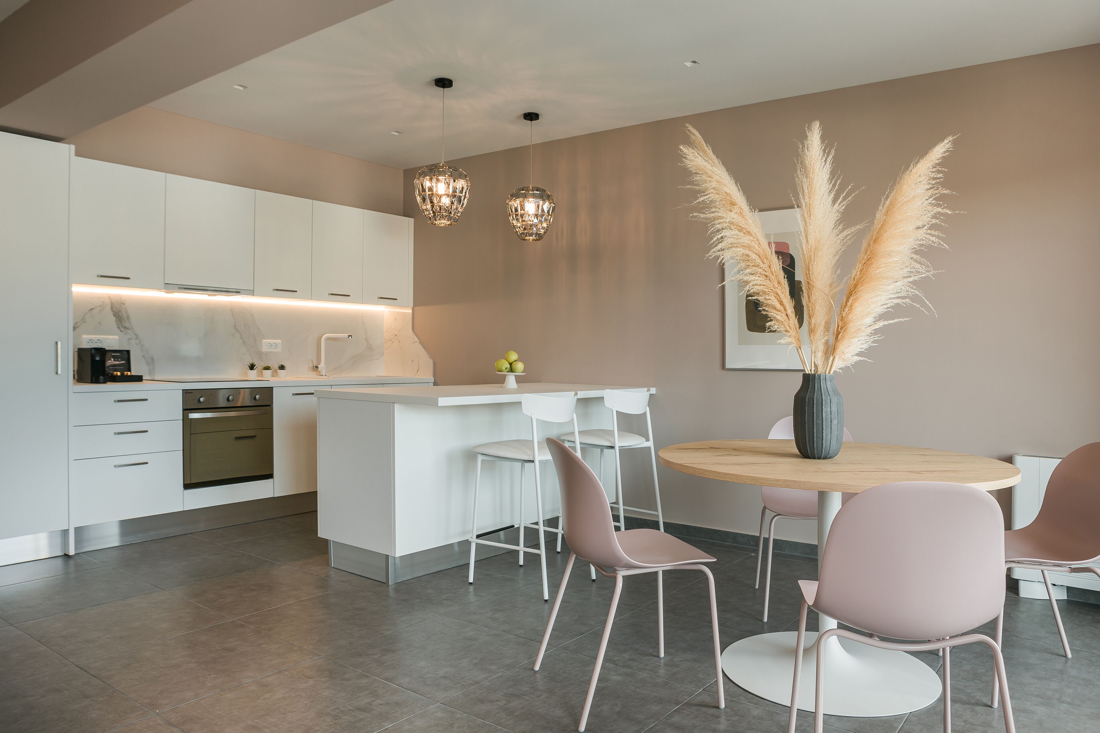A modern kitchen with white cabinets, a stainless steel oven, and a central island with chairs.