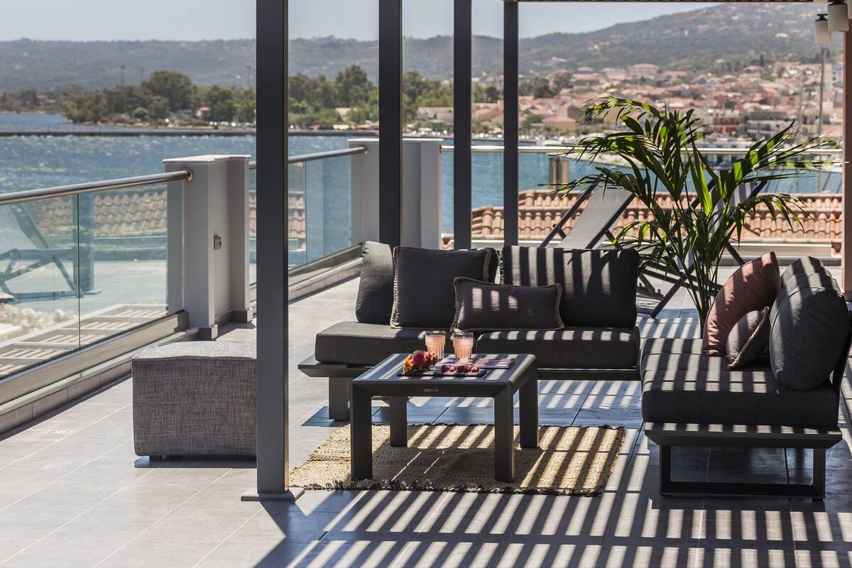 A terrace with outdoor seating, a table with drinks, and a view of the sea and town.