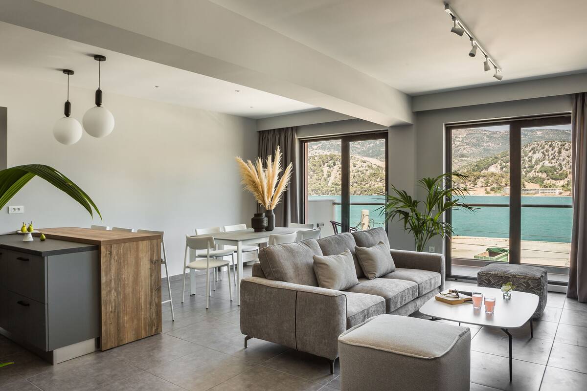 A modern living room with a grey sofa, a coffee table, and a dining area with white chairs.