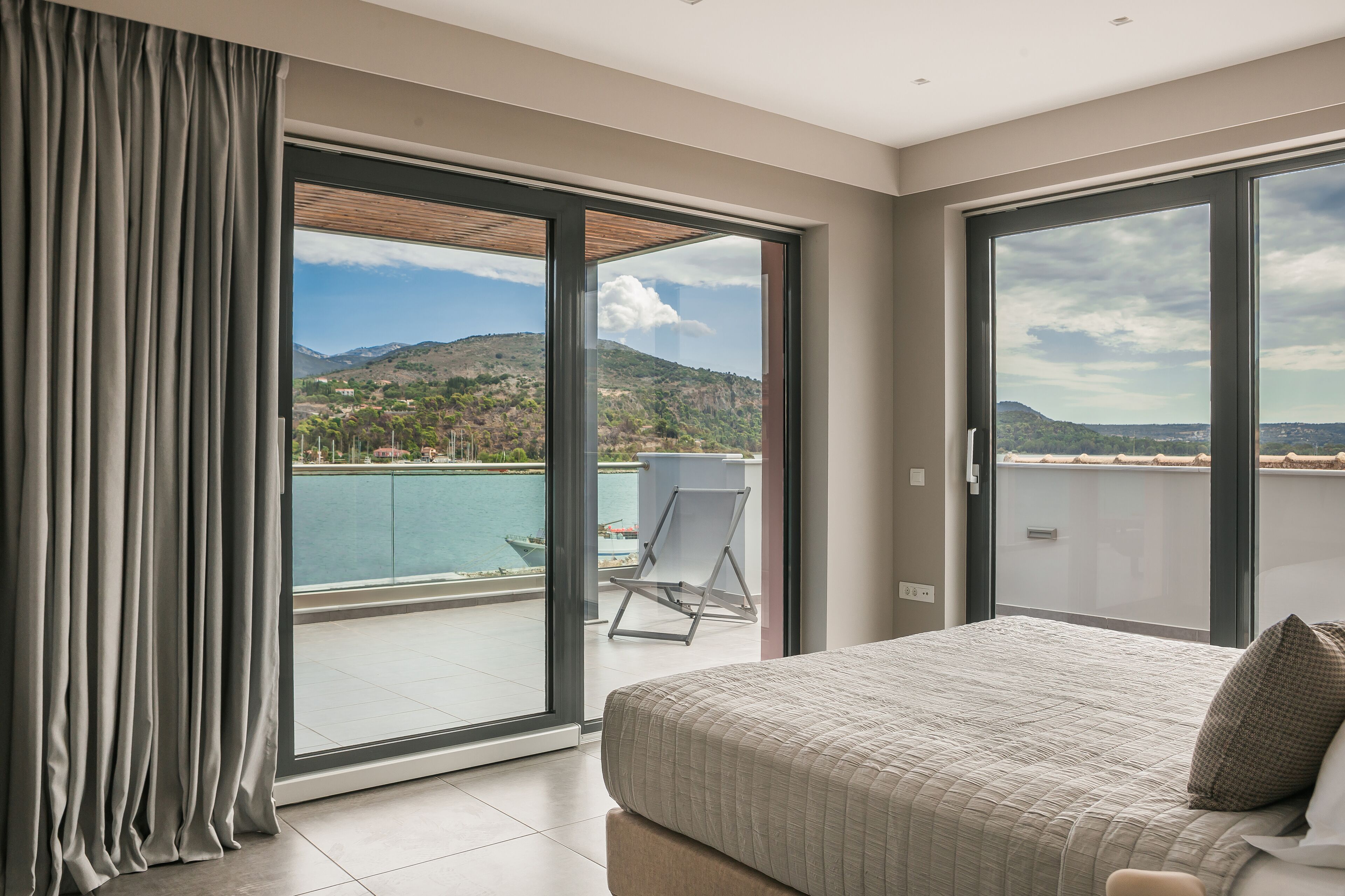 Ein Schlafzimmer mit großem Bett, Blick auf Pool und Berge sowie einer Schiebetür zu einem Außenbereich.