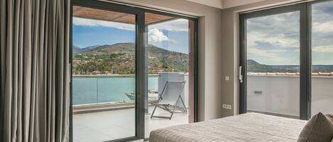 Ein Schlafzimmer mit großem Bett, Blick auf Pool und Berge sowie einer Schiebetür zu einem Außenbereich.
