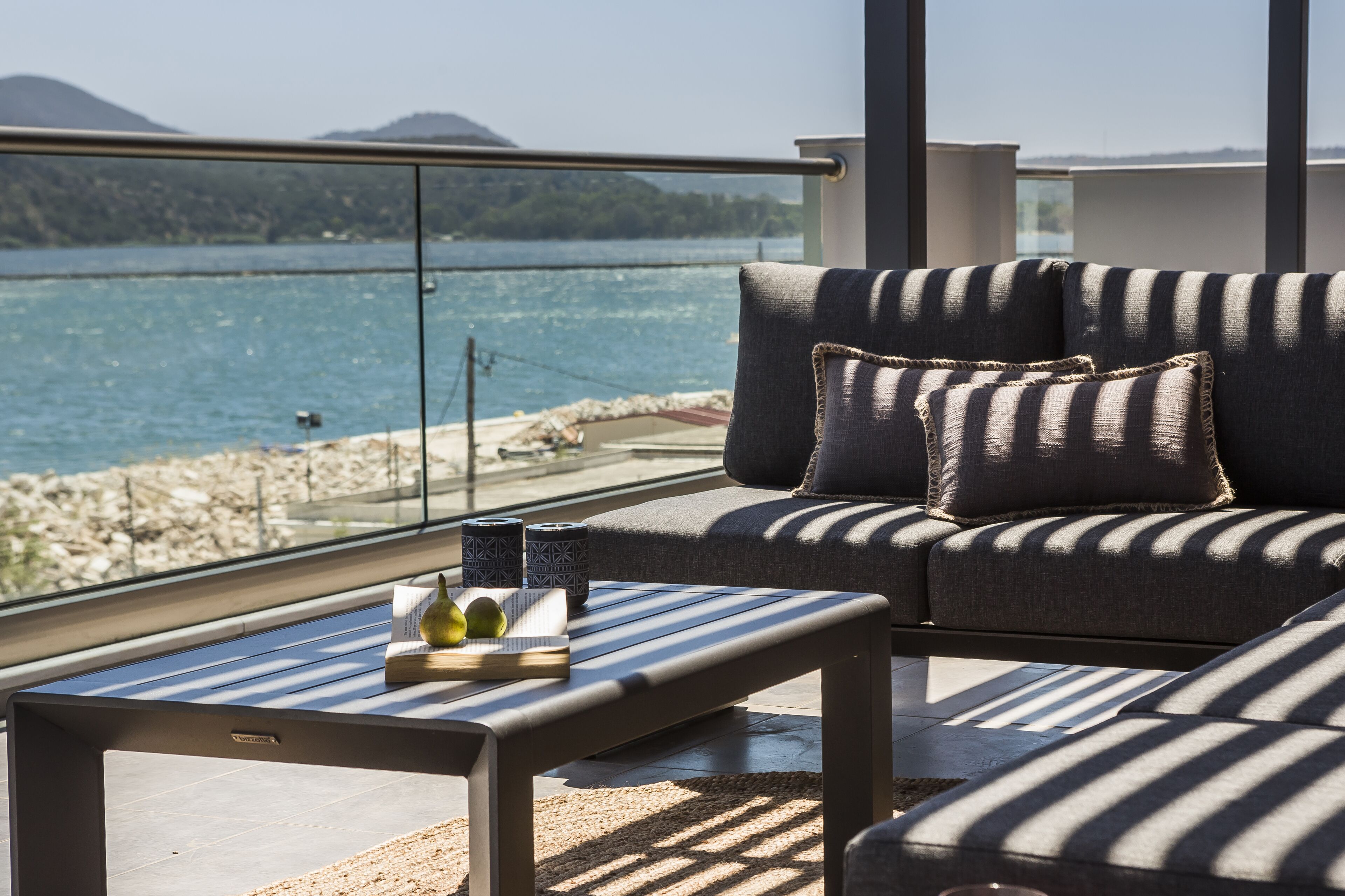 Ein Balkon mit einer Couch und einem Tisch, der auf ein Gewässer und eine felsige Küste blickt.