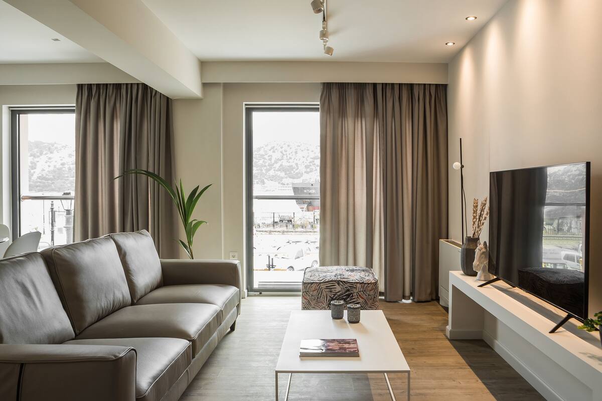 A modern living room with a leather sofa, a white coffee table, and a flat-screen TV mounted on the wall.