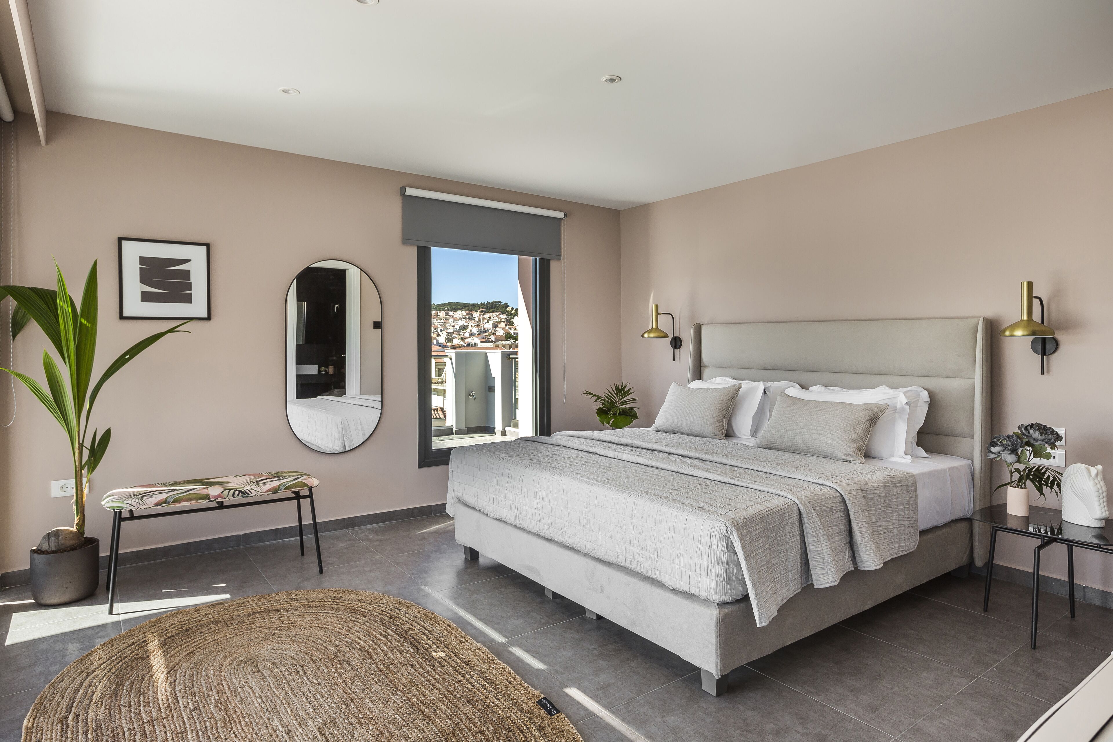 Un dormitorio moderno con una cama grande, un banco, una planta en maceta y vistas de la ciudad.
