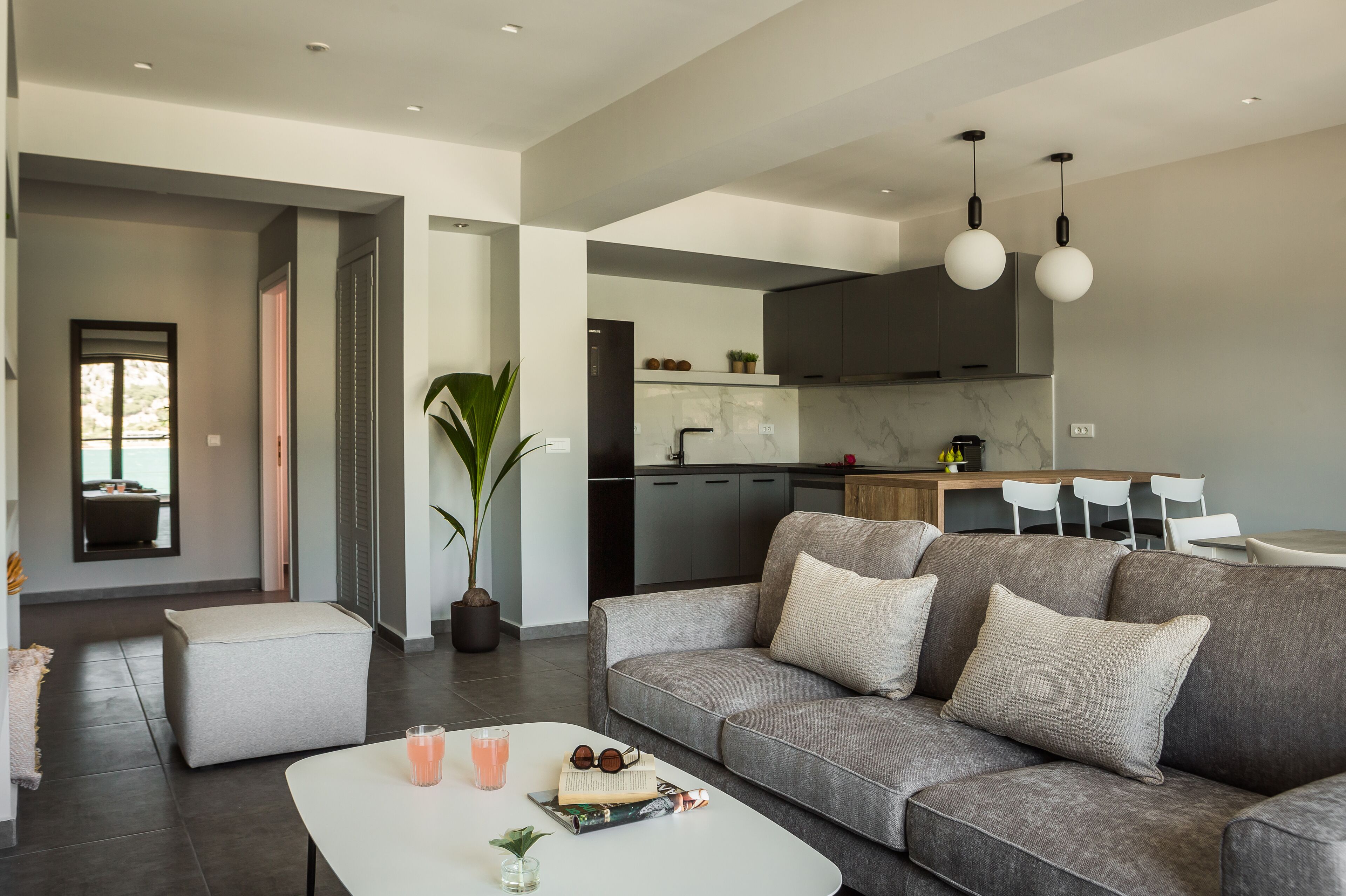 A modern living room with a grey sofa, a white coffee table, and a dining area with a white table and chairs.