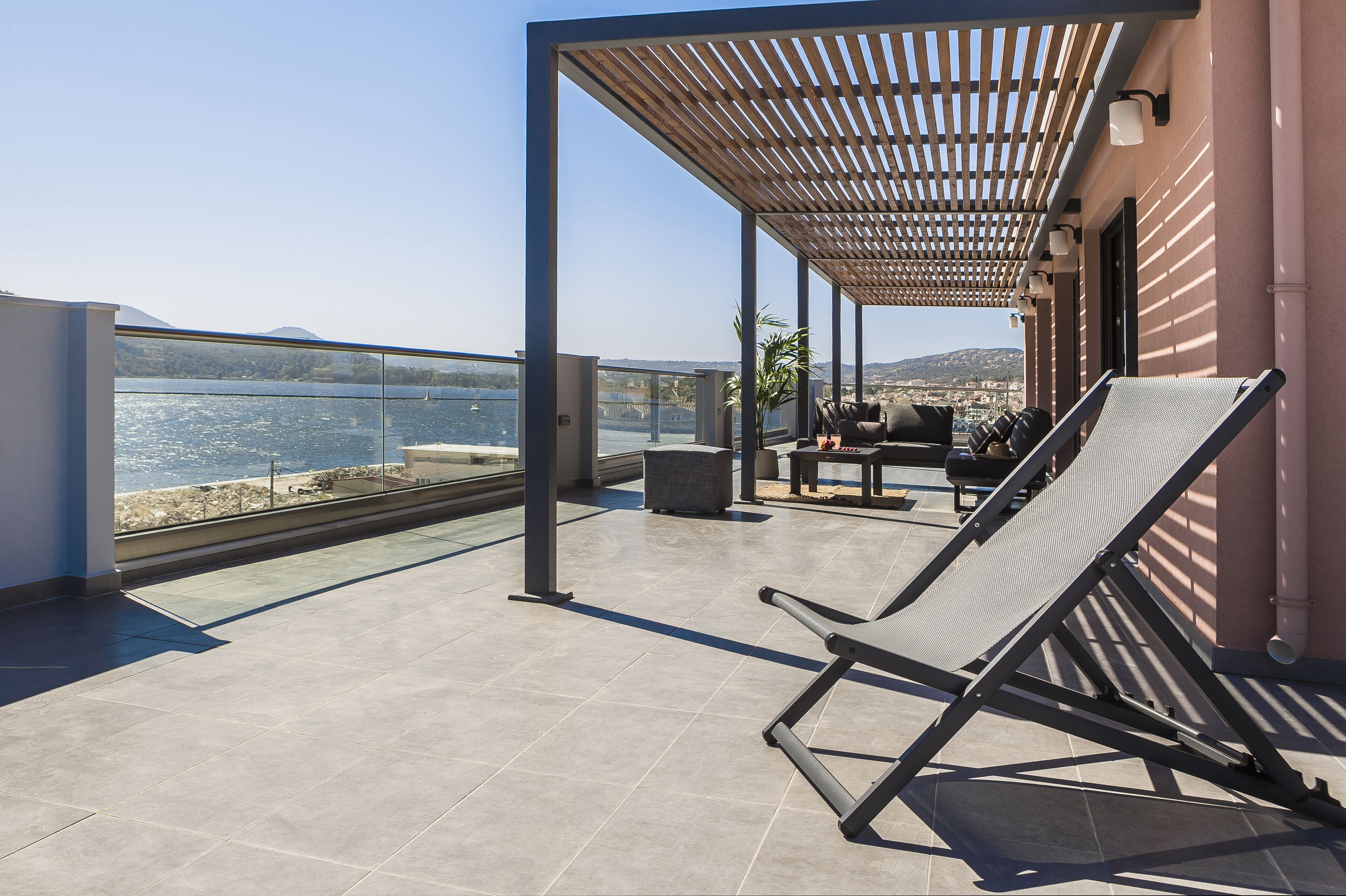 Uno spazio esterno coperto con vista sul mare, una poltrona da relax e un tavolo con sedie.
