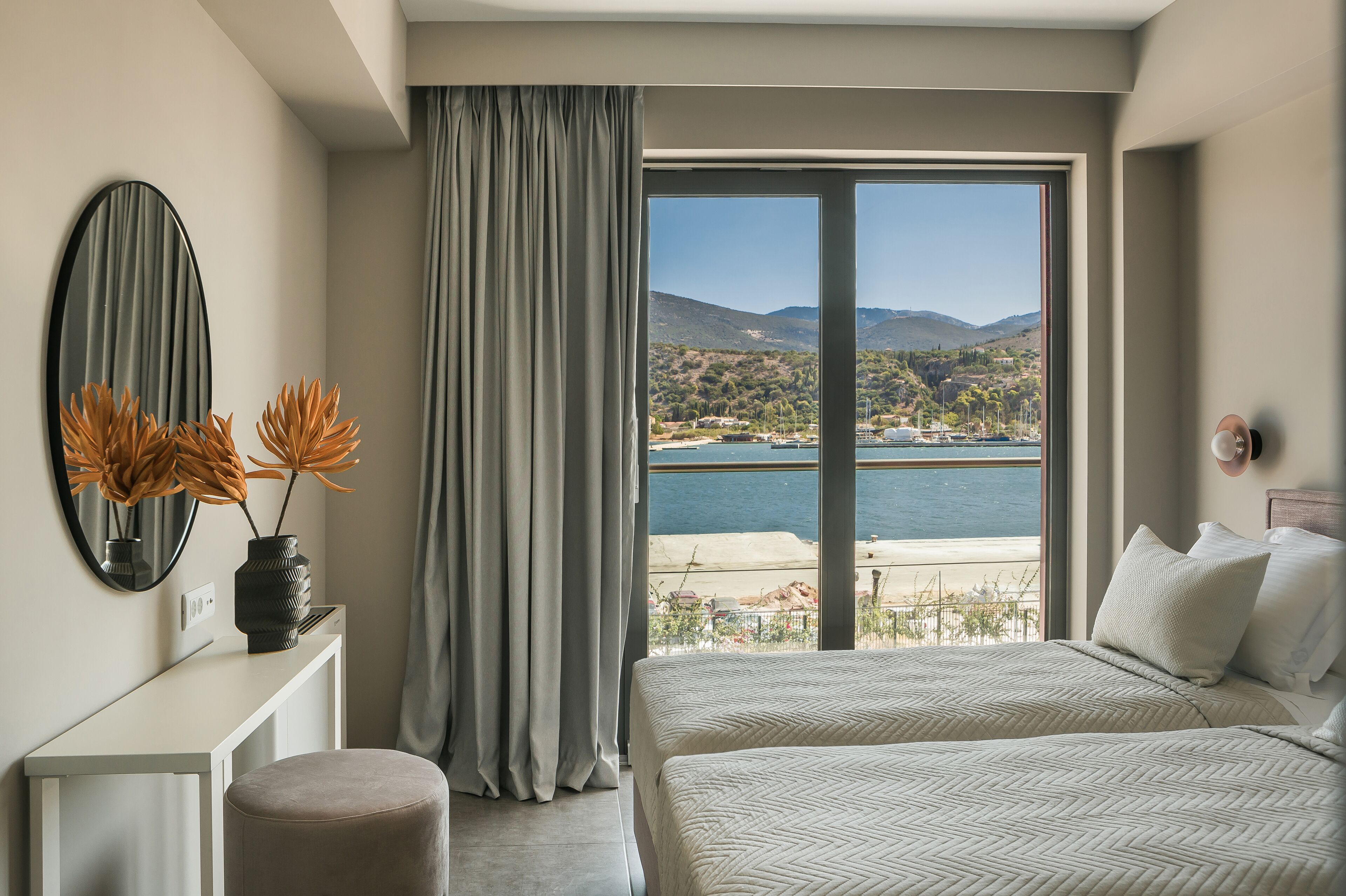 A hotel room with a large window, a bed, a bedside table, and a mirror.