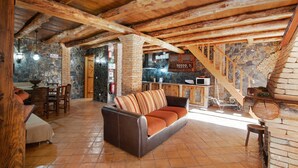 A rustic interior with exposed wooden beams, a stone wall, a fireplace, and a dining area.