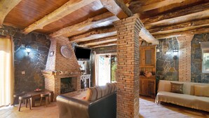 A rustic interior with exposed wooden beams, a stone fireplace, a leather sofa, and a stone wall.