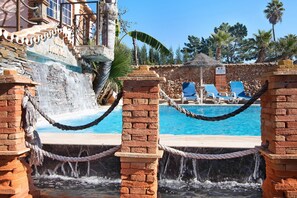 Zona de piscina amb cascada, gandules i mur de pedra.