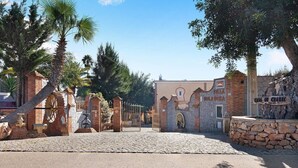 Een oprit met kinderkopjes, een poort, palmbomen en een gebouw met een stenen gevel en een bord waarop staat 'Hotel Casa de la Cultura'.