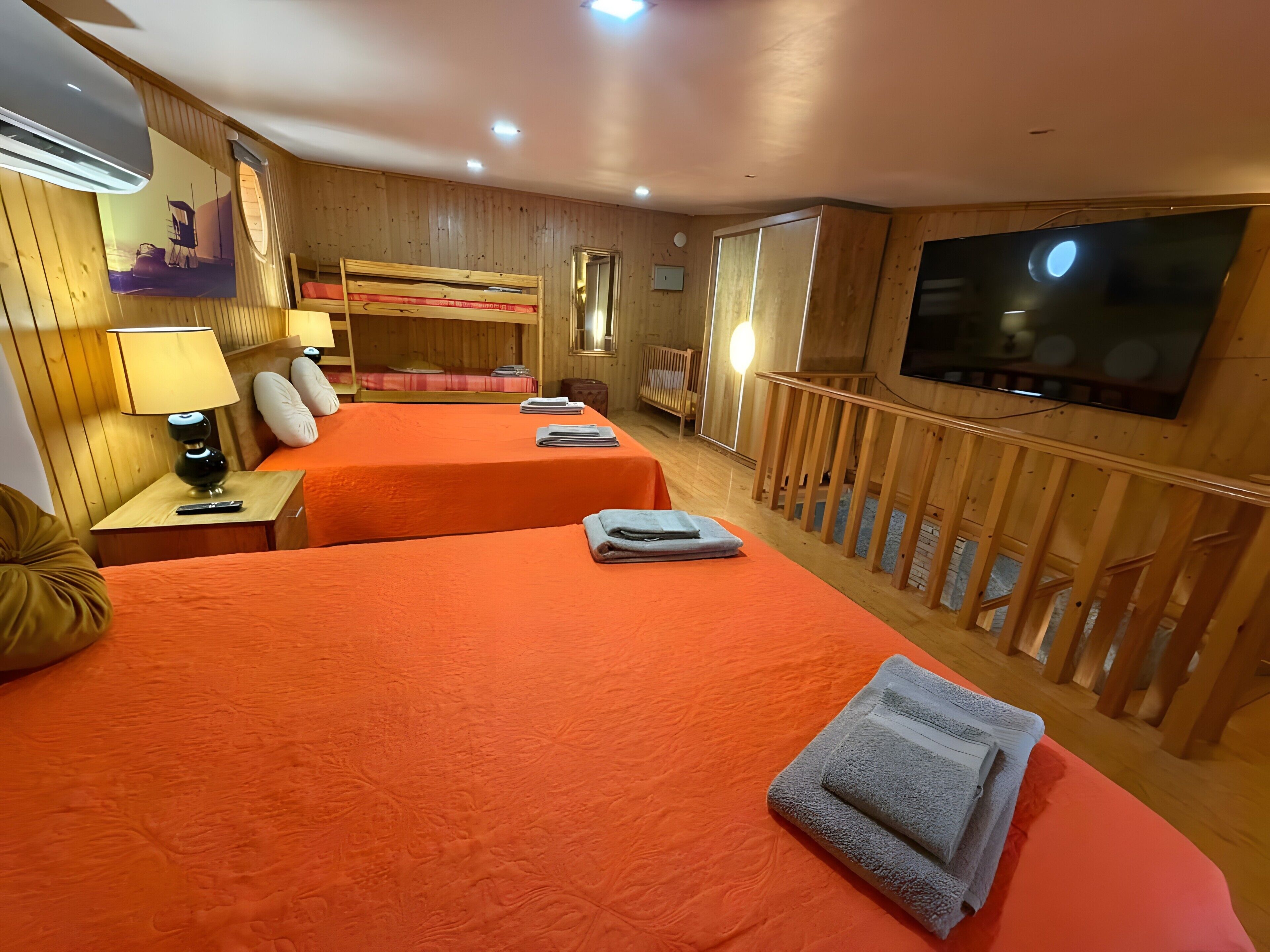 A room with two beds, a TV, a bunk bed, wooden walls, and a balcony.