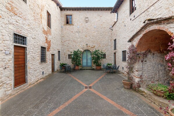 A courtyard with stone walls, a central door, and potted plants.