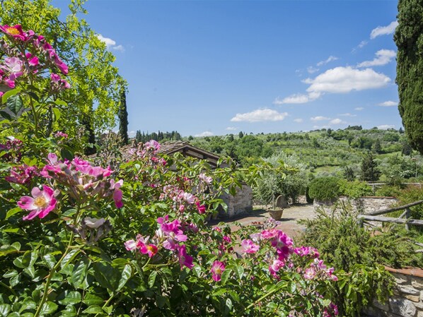 A rustic stone building surrounded by lush greenery and blooming pink flowers.