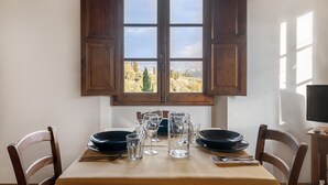 A dining table with chairs, a window with wooden shutters, and a view of greenery outside. - Agriturismo Il Melo with Mountain View, Shared Pool and Wi-Fi (Grassina)