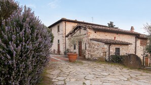 A stone building with a tiled roof, a stone courtyard, and a large potted plant. - Agriturismo Il Melo with Mountain View, Shared Pool and Wi-Fi (Grassina)