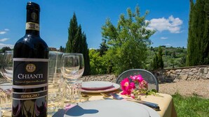 A table set outdoors with a bottle of Chianti wine, glasses, plates, and a chair with a flower. - Agriturismo Il Melo with Mountain View, Shared Pool and Wi-Fi (Grassina)