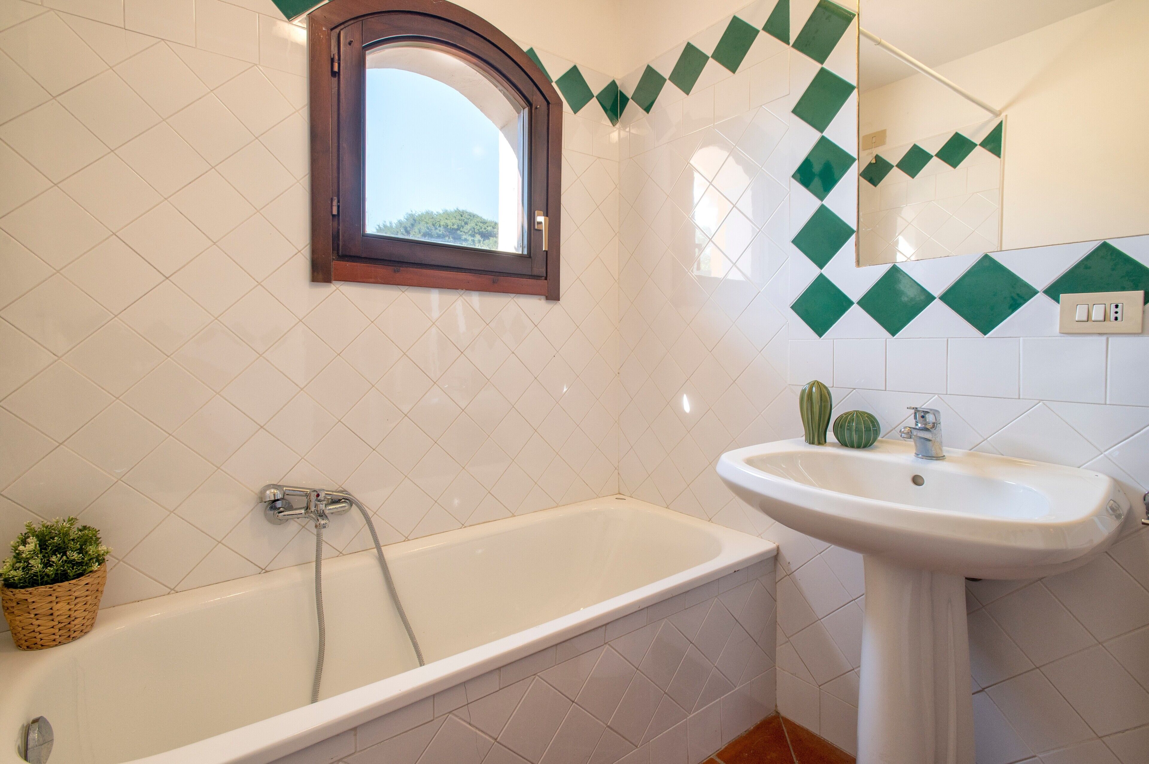 A bathroom with a bathtub, a sink, a window, and green diamond-patterned tiles.