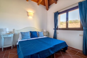 A bedroom with a bed, bedside tables, a window with curtains, and a ceiling with wooden beams.