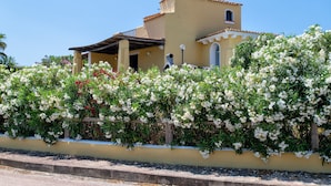 A building with a yellow facade, a small balcony, and a garden with white flowers. - Villa "Azzurra" with Sea View, Pool and Garden (Stintino)