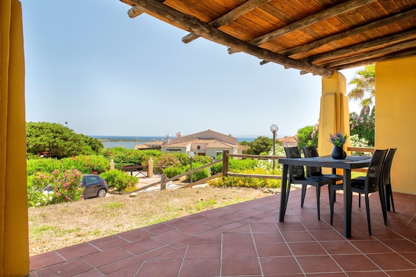 Eine Terrasse mit Tisch und Stühlen, Blick auf das Meer und ein Haus im Hintergrund.