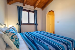Ein Schlafzimmer mit Bett, Vorhängen, einem Fenster und einer Rundbogenöffnung.