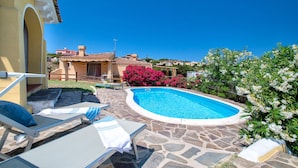 A swimming pool with lounge chairs, a stone patio, and a building with a tiled roof in the background. - Villa "Azzurra" with Sea View, Pool and Garden (Stintino)