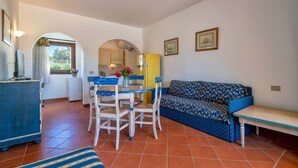 Een woonkamer met een bank, een eettafel met stoelen, een keukenhoek en een raam met gordijnen.