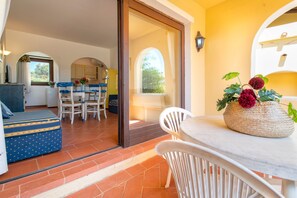 A room with a sliding glass door leading to a balcony, a dining area with a table and chairs, and a sofa with a patterned cover.