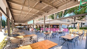 An outdoor café with wooden tables and chairs, a bar area, and a view of the surrounding trees. - Orka Village Hisarönü (Fethiye)