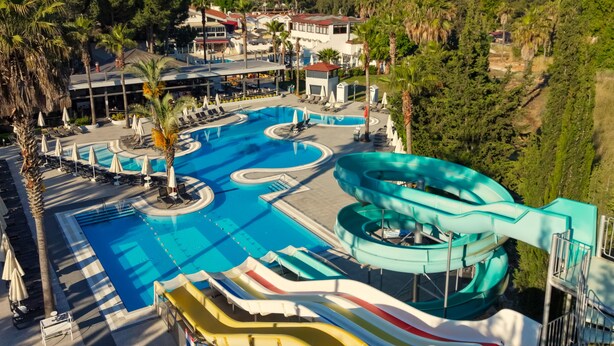 A resort with a large swimming pool, a water slide, and a view of a mountainous area. - Orka Village Hisarönü (Fethiye)