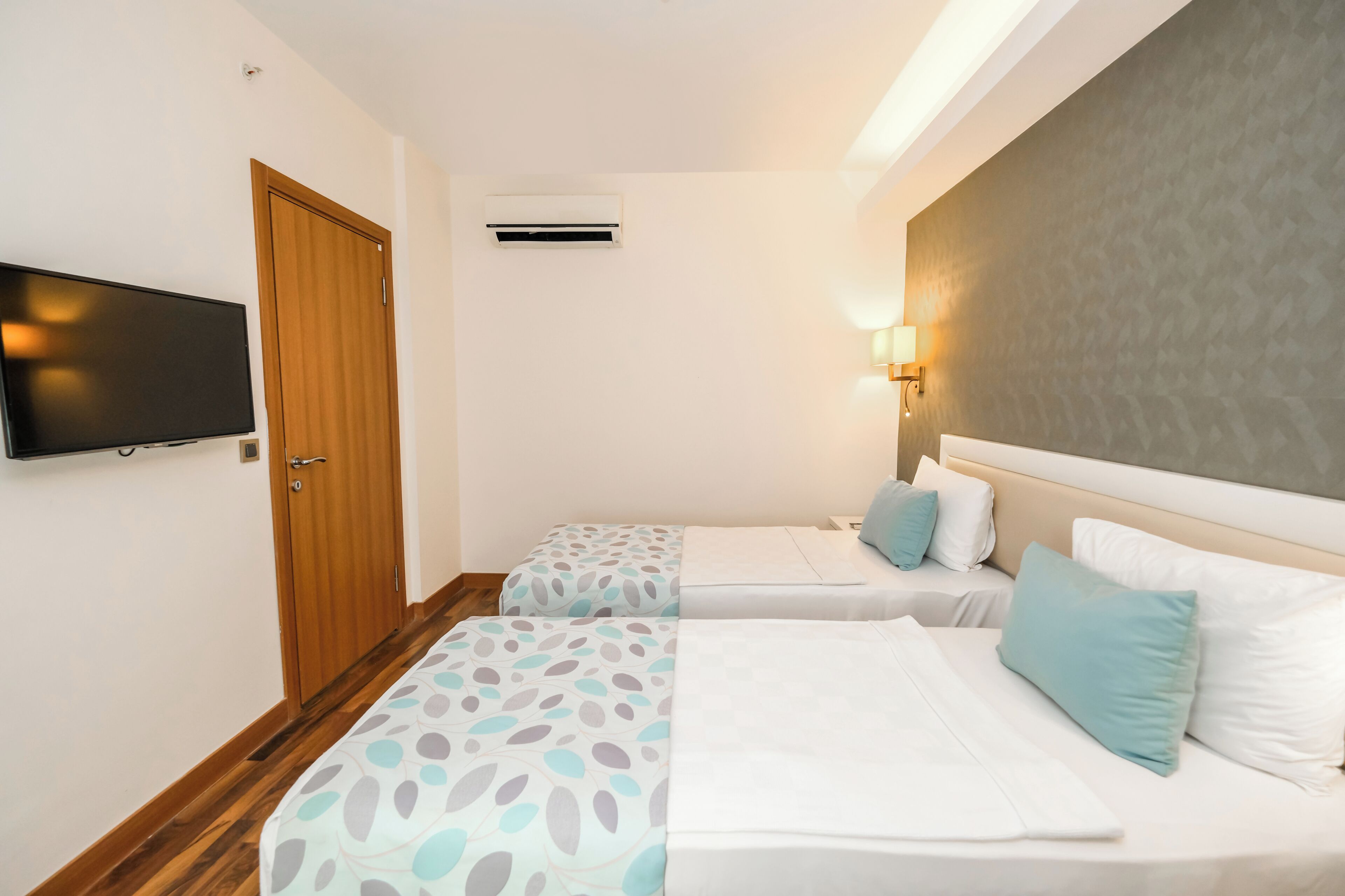 Une chambre d’hôtel avec deux lits, une télévision, un appareil de climatisation et une lampe fixée au mur.