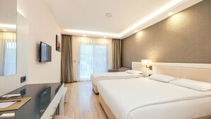 A hotel room with a large bed, a desk with a computer, a TV, and a window with curtains. - Orka Village Hisarönü (Fethiye)