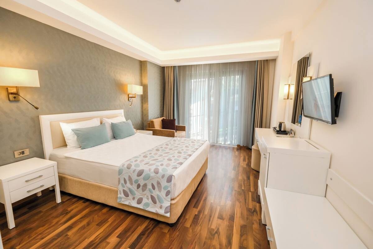 A hotel room with a large bed, bedside tables, a TV, and a desk.