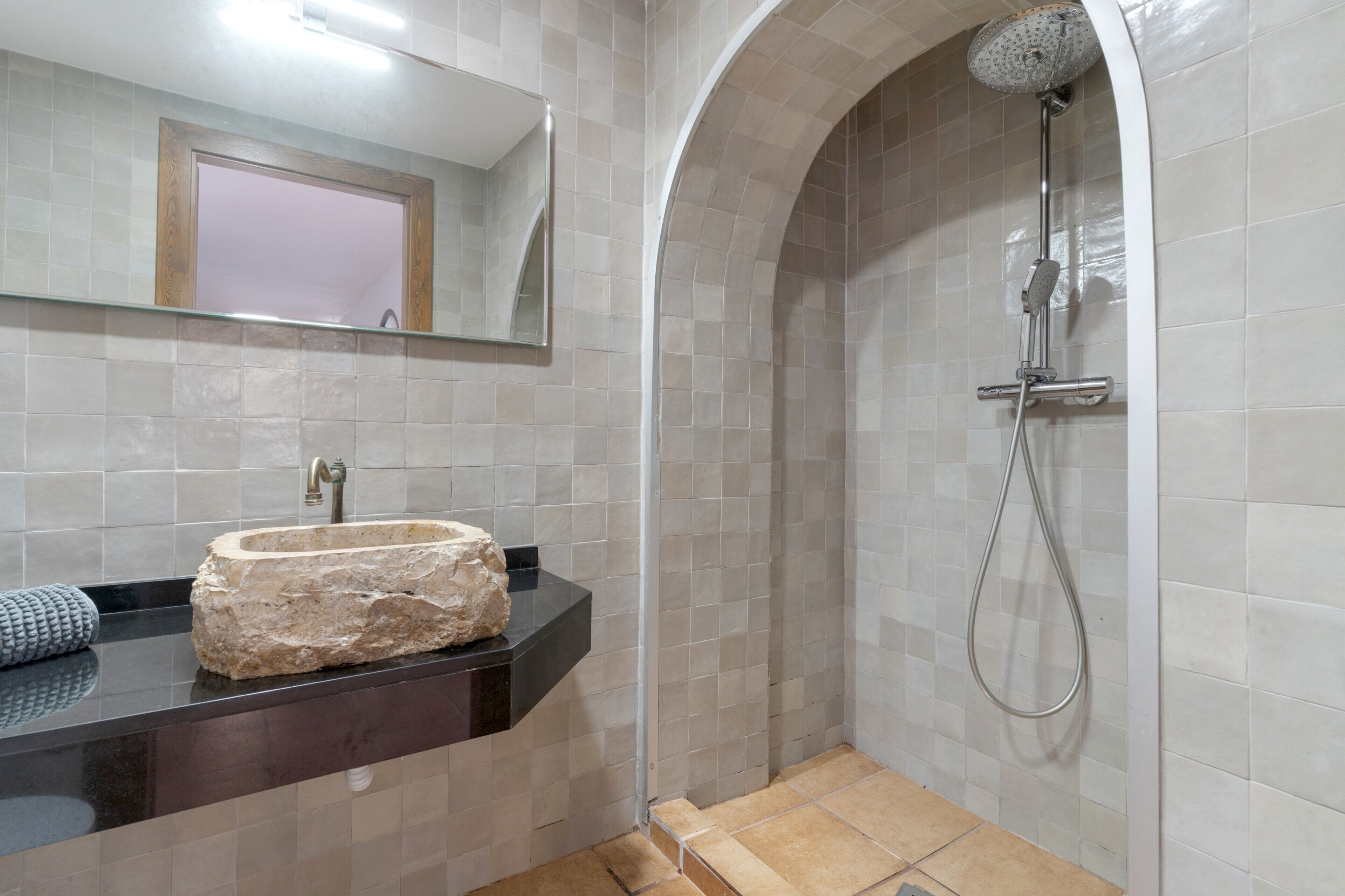 A bathroom with a stone sink, a shower with a handheld showerhead, and a mirror above the sink.