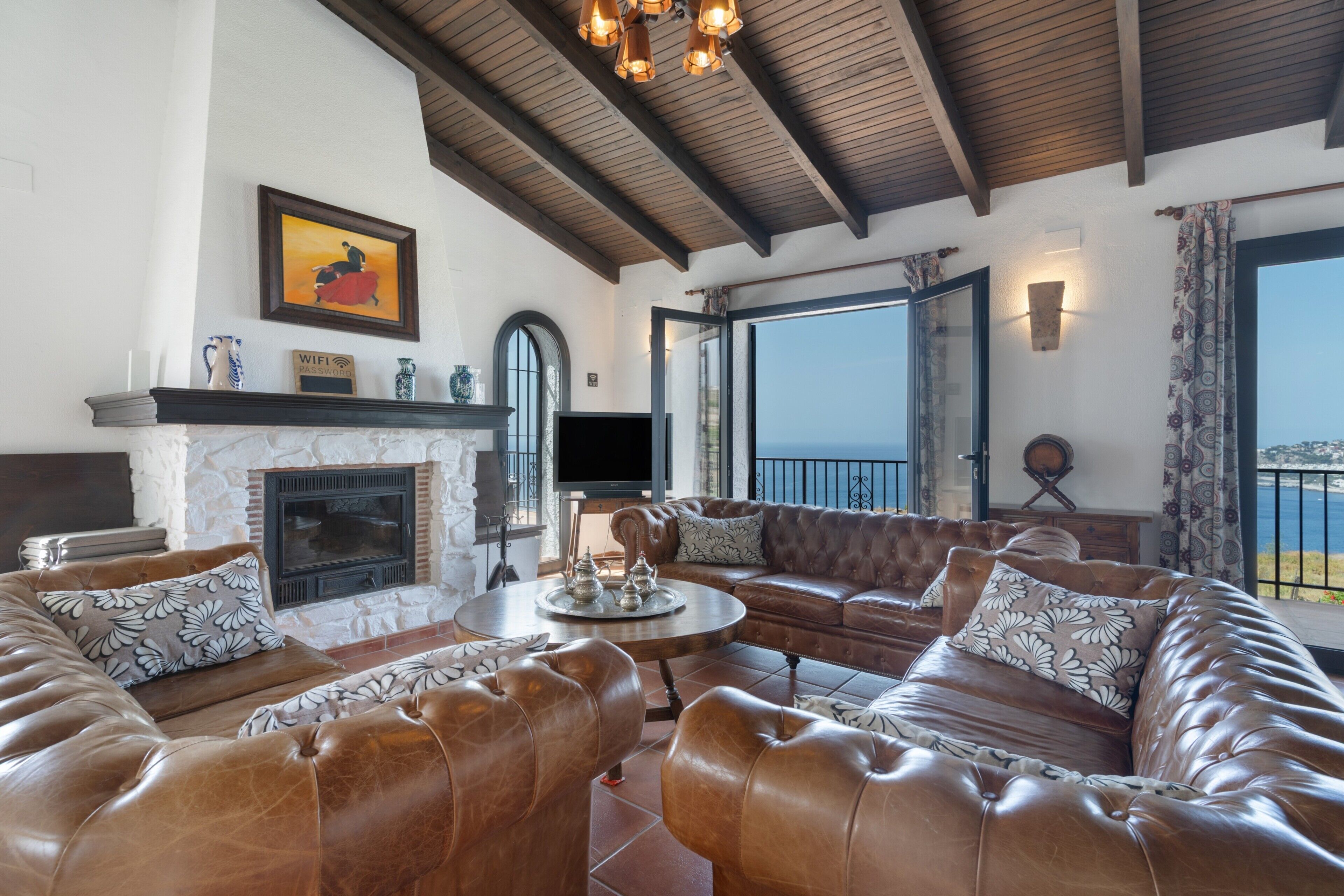A spacious living room with leather sofas, a fireplace, a television, and a balcony with a view.