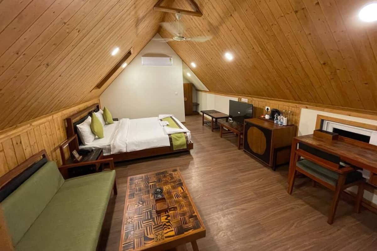 A cozy attic bedroom with a bed, a green sofa, a wooden coffee table, a desk with a chair, and a television.