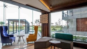 Eine moderne Lobby mit Glaswand, Holzboden und einer Beschilderung, die Einrichtungen wie ein Restaurant und ein Fitnessraum anzeigt.